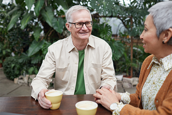 A senior man talks to a senior woman at a table outside.