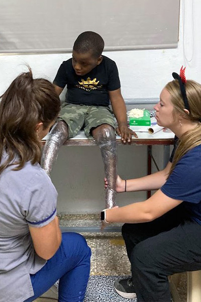 Shalese Evertsen and Alex Bushman wrap a pediatric patient's legs, preparing to cast a mold for new prosthetics.