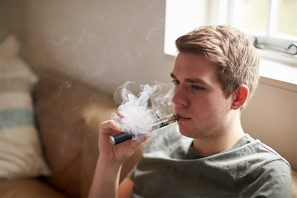 A young man breathes vapor from an electronic cigarette.