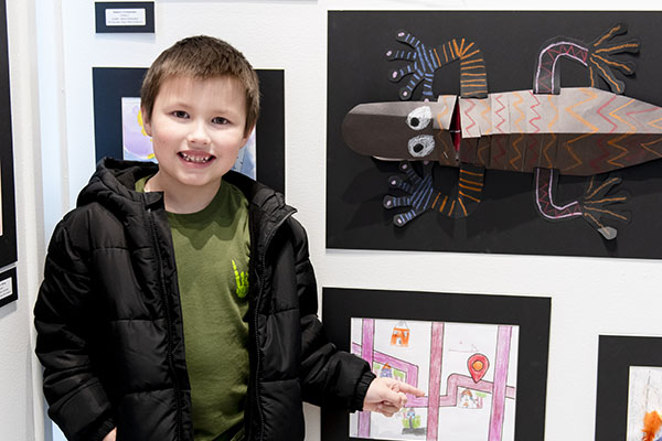 Grade school student poses with some art made by young students.