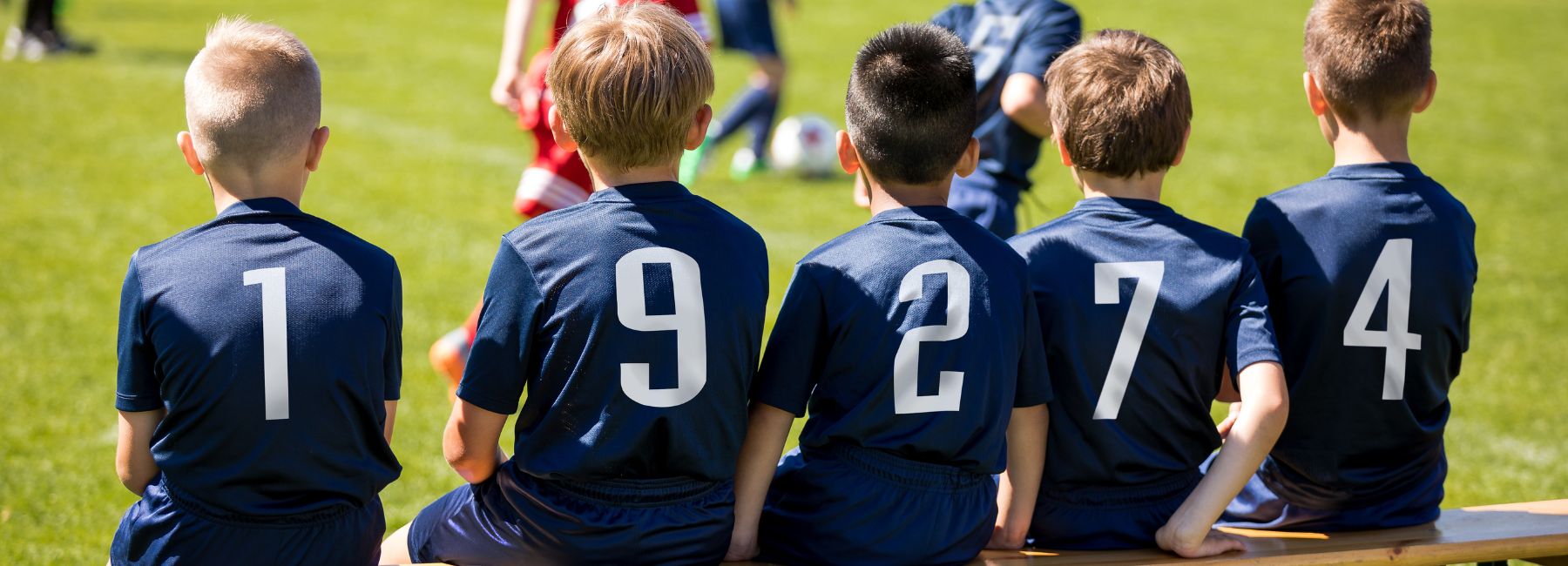 Four youth soccer players sitting on a bench during a game..
