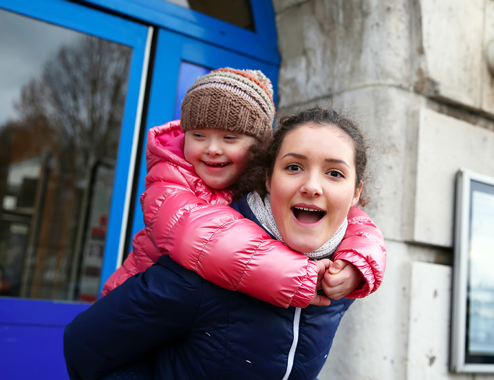 Student giving a young girl with disability a piggyback ride.
